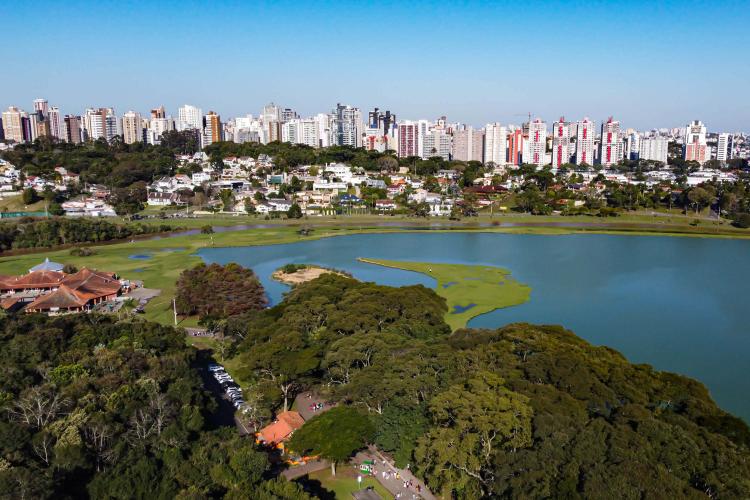 Imagem do Parque Barigui, um dos maiores e mais frequentados parques de Curitiba, simboliza a visão urbanística de Jaime Lerner, que priorizava a criação de espaços públicos integrados à natureza para o lazer e bem-estar da população. Projetado para ser um refúgio verde em meio à cidade, elaborado pelo arquiteto Lubomir Ficinski o parque também tinha o objetivo de conter enchentes e preservar a mata nativa da bacia do Rio Barigui.